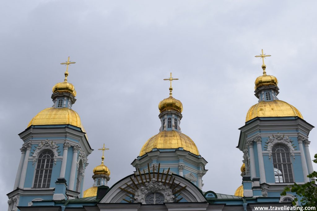 Aparecen 3 cúpulas doradas con una cruz encima y parte de la fachada azul y blanca de la iglesia.