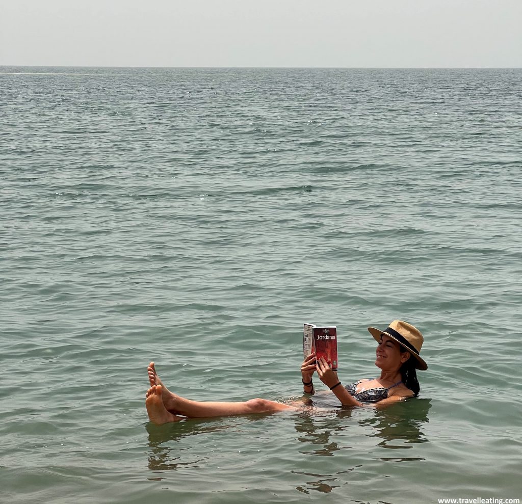 Chica flotando en el Mar Muerto mientras lee una guía con información para viajar por Jordania.