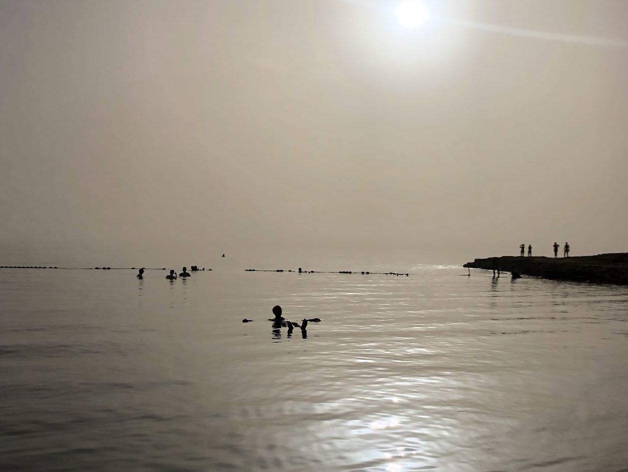 Chico flotando en el agua del Mar Muerto, con los brazos abiertos, bajo el sol del atardecer, que combinado con la calima ofrece estos sonos dorados tan espectaculares.