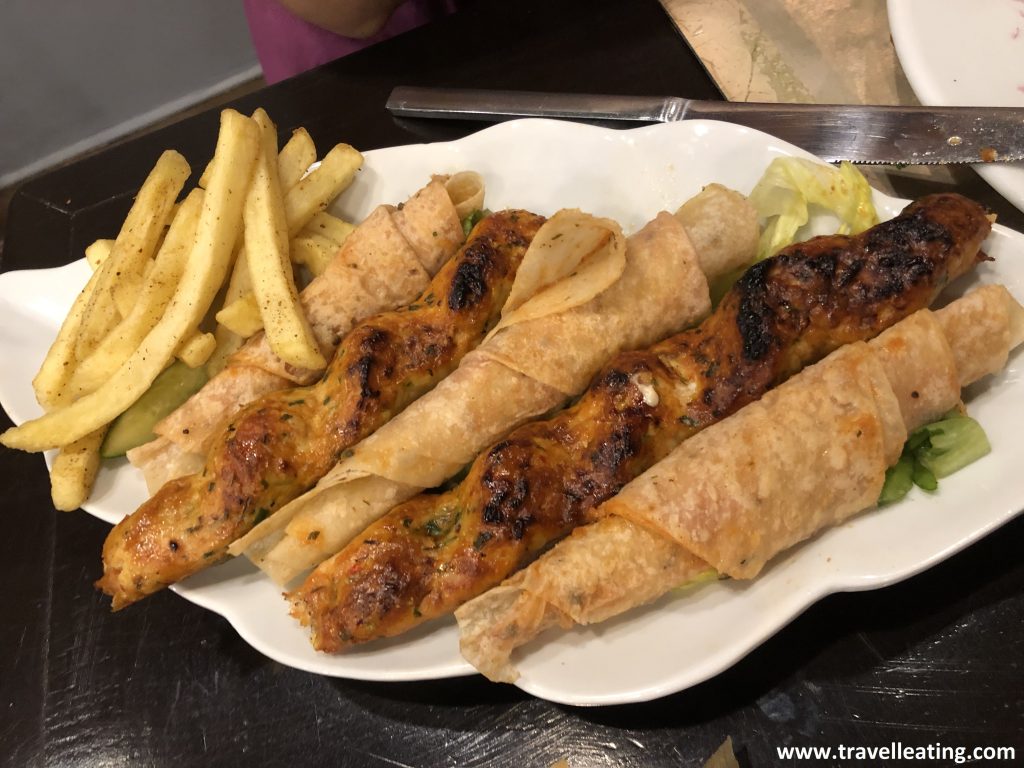 Plato que presenta dos pinchos de pollo con tres panes de pita enrollados y una patatas fritas de acompañamiento.