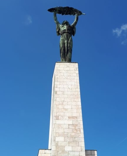 Monumento que presenta la estatua de una mujer alzando una pluma gigante con sus dos manos, encima de un obelisco.