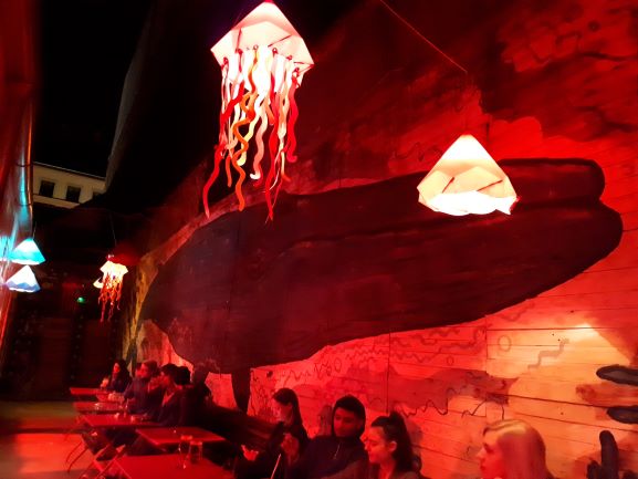 Pared de un bar con una enorme ballena pintada y unas luces rojas que representan medusas.