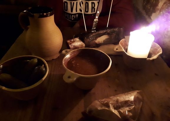 Mesa de un restaurante de estilo medieval, con un par de platos, dos cervezas y todo iluminado por velas.