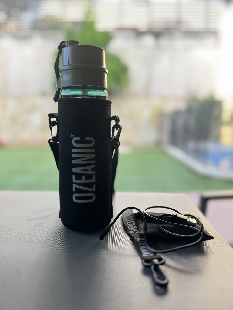 Cantimplora de agua Ozeanic, de color turquesa con una funda negra para colgársela y un cargador para el filtro de ozono.