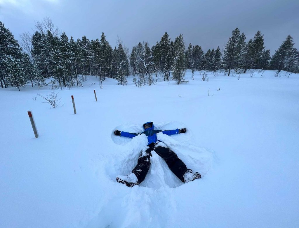 Chico estirado en la nieve, haciendo el ángel, con ropa impermeable. Un imprescindible al viajar a Tromso.